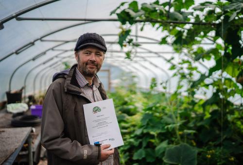 Man in polytunnel holding certificate